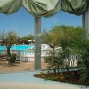 Vista da una finestra su una piscina circondata da piante e alberi.