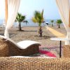Lounge in vimini sotto una pergola su una spiaggia, con pavimento in legno e palme intorno.