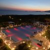 Piscina illuminata al tramonto con vista mare e luci rosse nell'acqua.