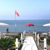 Passerella bianca su una spiaggia con ombrelloni e una bandiera rossa.