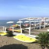 Spiaggia con cabine, lettini bianchi, ombrelloni e kayak gialli sulla sabbia, fronte mare.