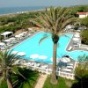 Una piscina circondata da palme, sdraio bianche e ombrelloni vicino alla spiaggia, vista dall'alto.