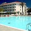 Piscina con sdraio e ombrelloni vicino a un grande edificio bianco con tetto rosso.
