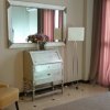 Camera d'albergo con poltrona beige, mobile vintage, specchio, lampada e tende rosa scuro.