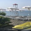 Spiaggia con ombrelloni bianchi, lettini e un pedalò giallo. Mare sullo sfondo.