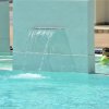 Bambino con braccioli verdi in una piscina vicino a una cascata d'acqua artificiale.