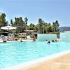 Piscina all'aperto con persone che nuotano e ombrelloni bianchi.
