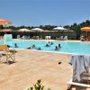 Piscina all'aperto con persone che nuotano, lettini e ombrelloni colorati attorno.
