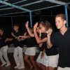Gruppo di persone che ballano su un palco, una persona tiene un microfono in mano.