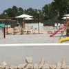 Parco giochi con scivolo e casetta, gazebo e sedie a sdraio sullo sfondo.