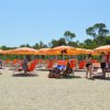Spiaggia sabbiosa con file di ombrelloni e sdraio arancioni. Persone rilassate sotto il sole.