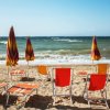 Sedie a sdraio multicolori e ombrelloni su una spiaggia sabbiosa con mare mosso.