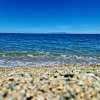 Una spiaggia con ciottoli in primo piano e un mare blu con un'isola all'orizzonte.