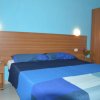 Camera da letto con parete blu, letto matrimoniale coperto da coperte blu e luci da comodino accese.