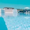 Piscina con acqua azzurra, ombrelloni bianchi e sedie a sdraio. Edificio sullo sfondo.