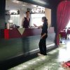 Un barista serve una cliente in un bar moderno con sedie arancioni e decorazioni rosse.