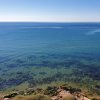 Mare calmo, acqua cristallina con variazioni di tonalità e costa rocciosa.