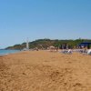 Spiaggia sabbiosa con lettini e ombrelloni, colline verdi sullo sfondo.