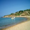 Una spiaggia sabbiosa con pedalò giallo e bianco in acqua. Una collina verdeggiante sullo sfondo.