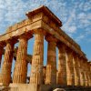 Tempio antico con colonne doriche sotto un cielo blu e nuvole sparse.