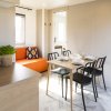 Sala da pranzo moderna con tavolo apparecchiato e sedute nere, divano arancione sullo sfondo.
