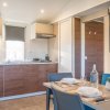 Cucina moderna con mobili in legno, tavolo apparecchiato, e una finestra con tende grigie.