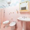 Bagno con piastrelle rosa, sanitari, lavandino e specchio giallo.