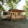 Una casa mobile con veranda in legno chiaro situata tra alberi verdi.