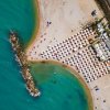 Spiaggia con ombrelloni disposti ordinatamente, una barriera di pietre e mare azzurro.