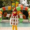 Una mascotte a forma di gallo davanti a scivoli d'acqua colorati.