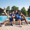 Tre persone sorridenti in abbigliamento sportivo blu sedute sul bordo di una piscina.