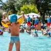 Bambini con braccioli gialli e cuffie azzurre in piscina, mentre istruttori guidano un'attività.