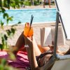 Una persona su un lettino, con un libro e un cocktail arancione in mano, accanto a una piscina.