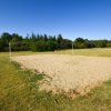 Campo da beach volley su un prato verde con alberi sullo sfondo.