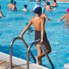 Bambino con costume e cuffia osserva un gruppo che nuota in piscina.