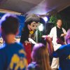 Persona in costume simpatico saluta bambini su un palco all'aperto.