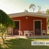 Piccola casa rossa con sedie bianche su un patio in un giardino verde.