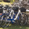 Biciclette con cestini nere parcheggiate sull'erba accanto a un muretto di pietra.