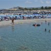 Spiaggia affollata con sedie a sdraio e ombrelloni.