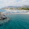 Spiaggia con ombrelloni blu, mare e colline sullo sfondo.