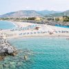 Spiaggia con ombrelloni blu e sedie a sdraio, vista mare e montagne.