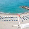 Spiaggia con sdraio e ombrelloni bianchi, mare e scogli sullo sfondo.