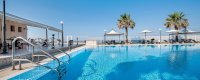 Piscina all'aperto con lettini e ombrelloni, palme sullo sfondo.