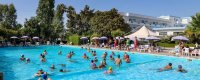 Piscina con molte persone che nuotano, circondata da ombrelloni e sedie.