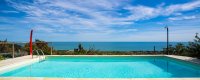 Piscina e mare sullo sfondo, cielo parzialmente nuvoloso.