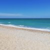 Spiaggia sabbiosa con mare azzurro e scogliere bianche in lontananza.
