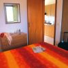 Interno di una camera con letto rosso e arancione, vista su un angolo cucina.