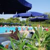 Piscina all'aperto con lettini e ombrelloni blu, circondata da vegetazione e fiori rosa.