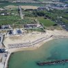 Spiaggia sabbiosa con ombrelloni e dintorni verdi.