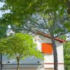 Casa bianca con imposte arancioni tra gli alberi.